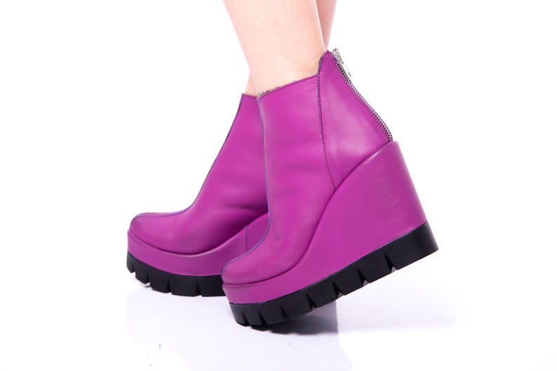 May include: A pair of purple wedge heeled ankle boots with a zipper on the back. The boots are made of leather and have a chunky platform.