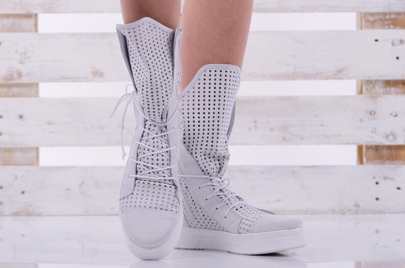 May include: White perforated leather ankle boots with laces. The boots have a thick white sole and are shown on a white wooden background.
