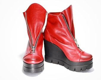 May include: A pair of red leather wedge boots with a zipper up the front of each boot.