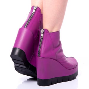 May include: A pair of purple wedge ankle boots with a zipper on the back of each boot.