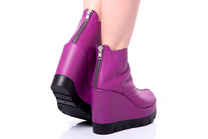 May include: A pair of purple wedge ankle boots with a zipper on the back of each boot.