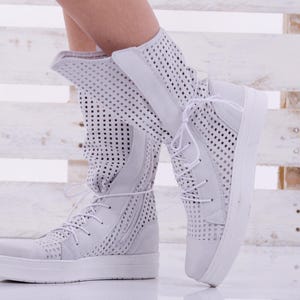May include: White high-top sneakers with a perforated design and white laces. The sneakers have a thick white sole.