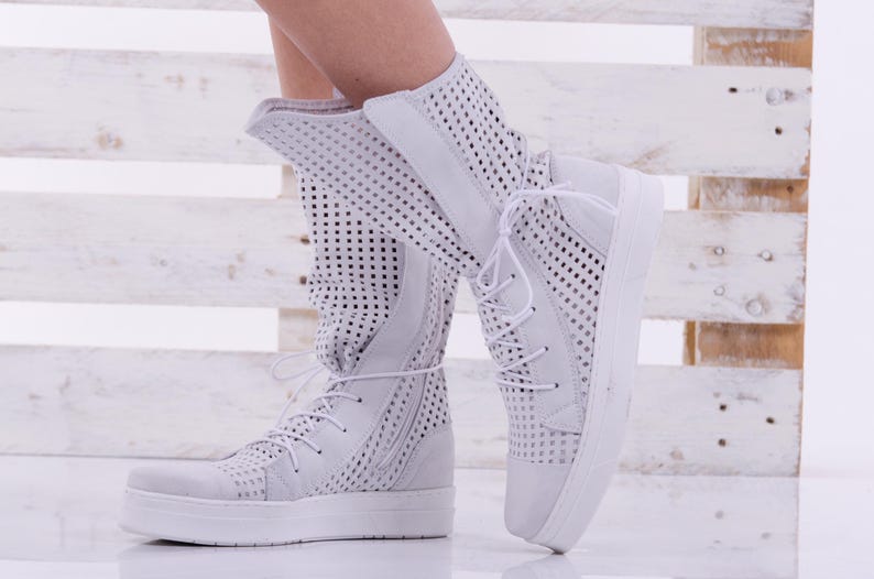 May include: White high-top sneakers with a perforated design and white laces. The sneakers have a thick white sole.