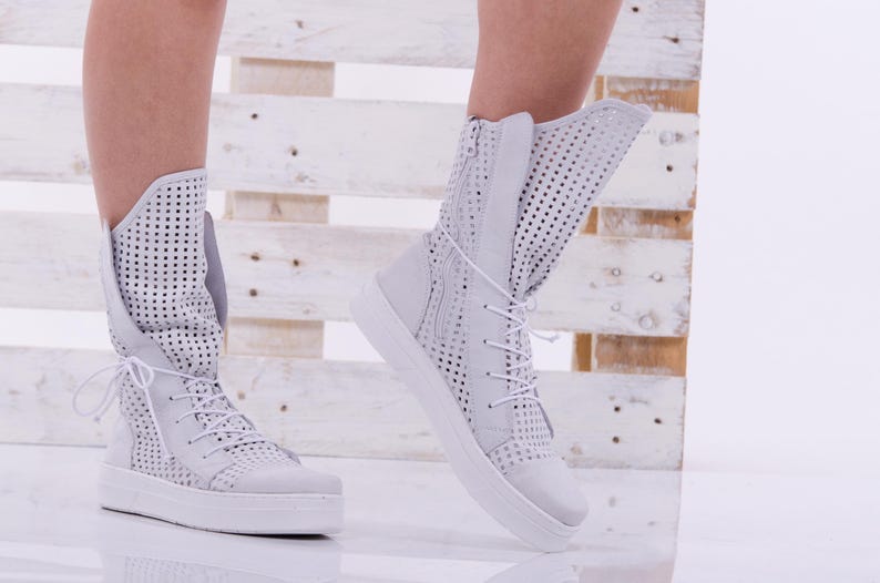 May include: White perforated leather ankle boots with laces. The boots have a thick white sole and are shown on a model's feet.