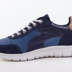 Op de afbeelding: Blauwe en bruine su&egrave;de sneakers met witte veters en een witte zool.