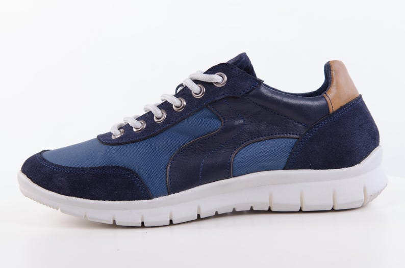 Op de afbeelding: Blauwe en bruine su&egrave;de sneakers met witte veters en een witte zool.