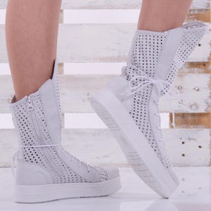 May include: White high-top sneakers with a perforated design and a zipper on the side. The sneakers have a thick white sole and are made of a soft, breathable material.