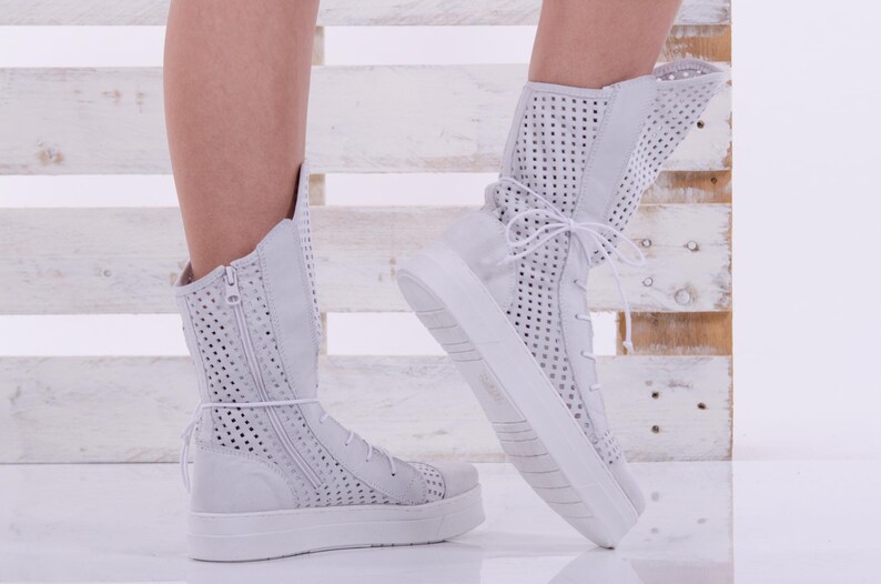 May include: White high-top sneakers with a perforated design and a zipper on the side. The sneakers have a thick white sole and are made of a soft, breathable material.