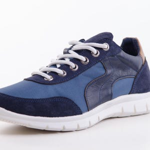Op de afbeelding: Een paar blauwe en donkerblauwe sneakers met witte veters en een witte zool.