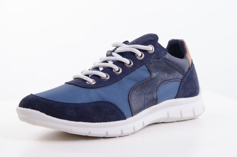Op de afbeelding: Een paar blauwe en donkerblauwe sneakers met witte veters en een witte zool.
