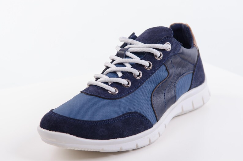 Op de afbeelding: Een paar blauwe en donkerblauwe sneakers met witte veters. De sneakers hebben een witte zool en een blauwe en donkerblauwe bovenkant.