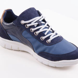 Op de afbeelding: Blauwe en marineblauwe sneakers met witte veters. De schoenen hebben een witte zool en een bruin lederen accent aan de achterkant.