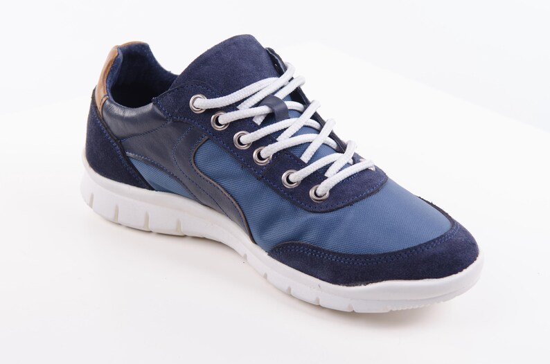 Op de afbeelding: Blauwe en marineblauwe sneakers met witte veters. De schoenen hebben een witte zool en een bruin lederen accent aan de achterkant.