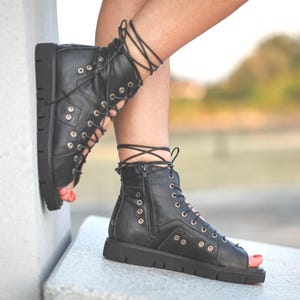 Könnte beinhalten: Schwarze Leder-Gladiator-Sandalen mit Schnürungen am Bein und einer dicken Plateau-Sohle.
