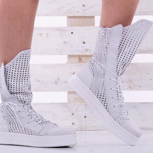 May include: White high-top sneakers with a perforated design and a white rubber sole.