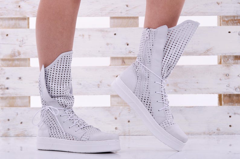 May include: White high-top sneakers with a perforated design and a white rubber sole.