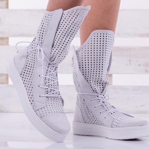 May include: White leather ankle boots with a perforated design and white laces. The boots have a chunky white sole.