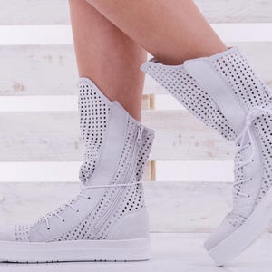 May include: White high-top sneakers with a perforated design and a zipper on the side. The sneakers have a white rubber sole.