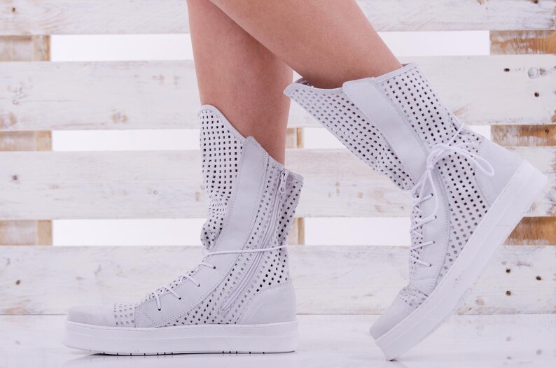 May include: White high-top sneakers with a perforated design and a zipper on the side. The sneakers have a white rubber sole.