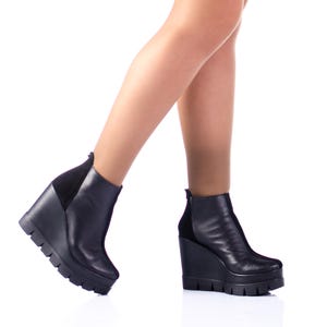 Könnte beinhalten: Ein Paar schwarze Lederstiefeletten mit Keilabsatz. Die Stiefeletten haben ein Wildlederpanel an der Rückseite des Knöchels.