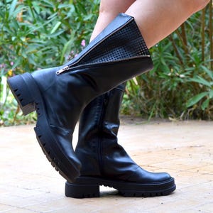 K&ouml;nnte beinhalten: Schwarze Lederstiefel mit seitlichem Rei&szlig;verschluss und einer dicken Plateau-Sohle. Die Stiefel haben ein Mesh-Panel an der Seite.