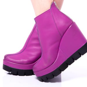 May include: A pair of purple platform wedge boots with a zipper on the back. The boots are made of leather and have a chunky platform sole.