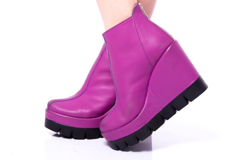 May include: A pair of purple platform wedge boots with a zipper on the back. The boots are made of leather and have a chunky platform sole.