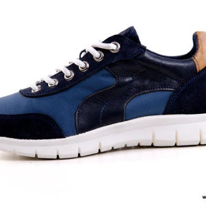 Op de afbeelding: Een paar blauwe en bruine sneakers met een witte zool. De sneakers hebben een su&egrave;de neus en een canvas bovenwerk.