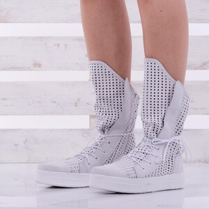 May include: White high-top sneakers with a perforated design and white laces. The sneakers have a white rubber sole.