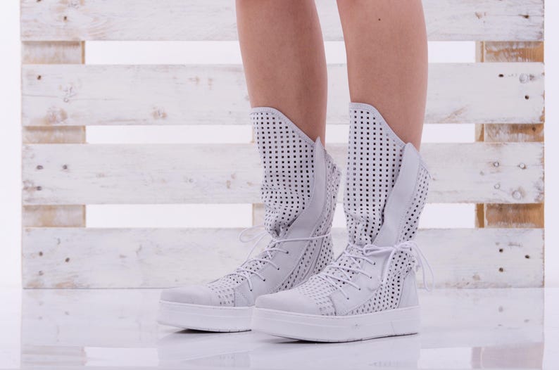 May include: White high-top sneakers with a perforated design and white laces. The sneakers have a white rubber sole.