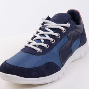 Op de afbeelding: Een paar blauwe en donkerblauwe sneakers met witte veters en een witte zool.