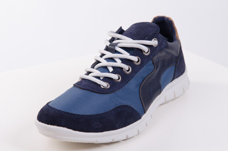 Op de afbeelding: Een paar blauwe en donkerblauwe sneakers met witte veters en een witte zool.
