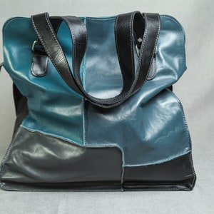 May include: A large, blue and black leather tote bag with two black leather handles.