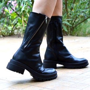 K&ouml;nnte beinhalten: Schwarze Lederstiefel mit einem dicken Absatz und einem seitlichen Rei&szlig;verschluss. Die Stiefel haben eine leicht spitz zulaufende Spitze.
