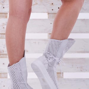 May include: White high-top sneakers with a perforated design and a zipper detail. The sneakers have a thick white sole and are made of a breathable material.