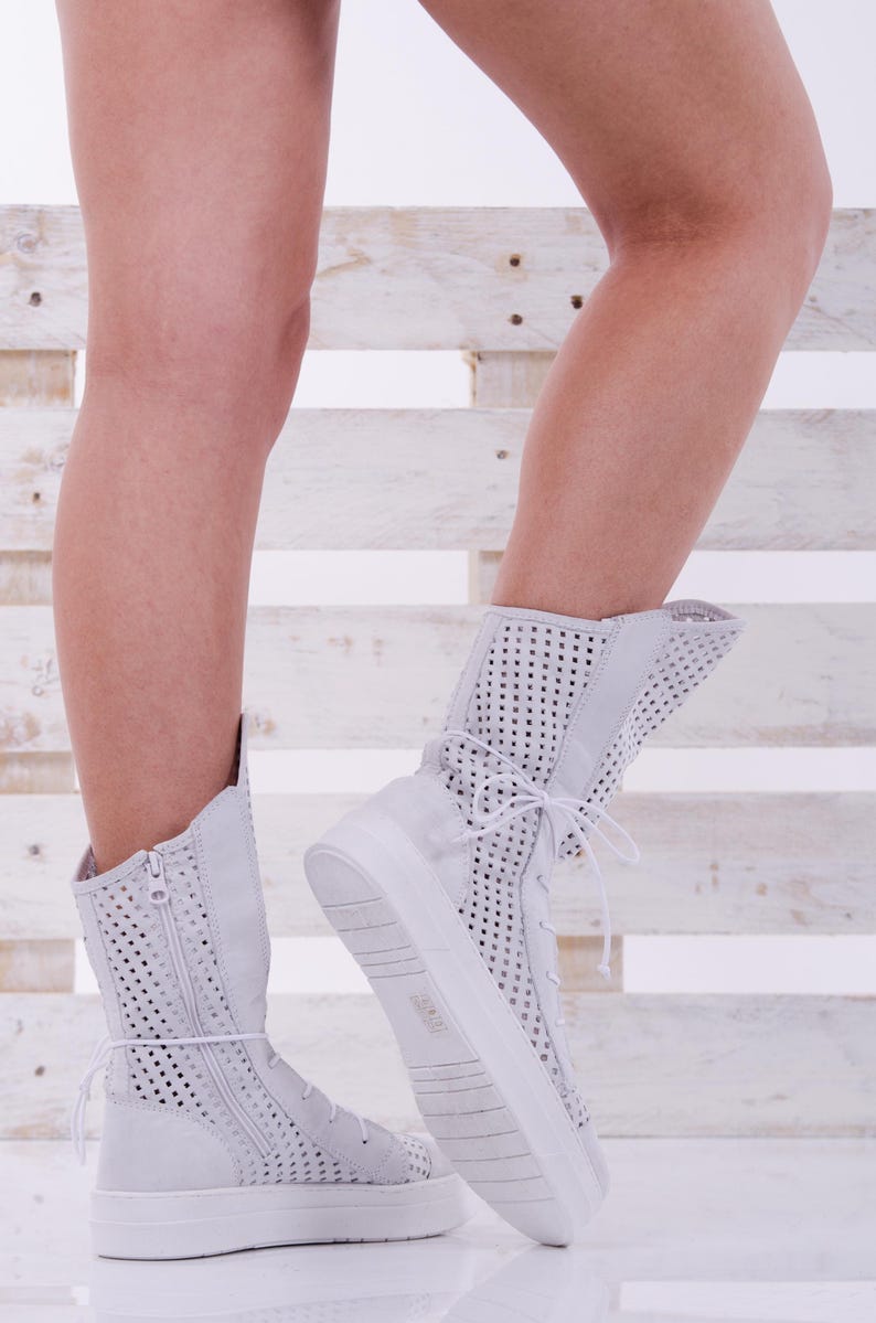 May include: White high-top sneakers with a perforated design and a zipper detail. The sneakers have a thick white sole and are made of a breathable material.
