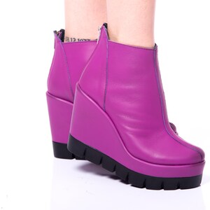 May include: A pair of purple wedge heeled ankle boots with a zipper on the back.