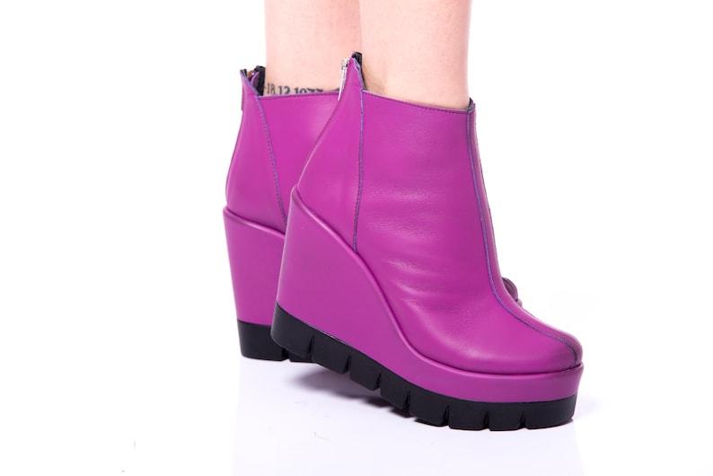 May include: A pair of purple wedge heeled ankle boots with a zipper on the back.