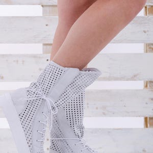 May include: White perforated leather ankle boots with white laces and a white rubber sole.
