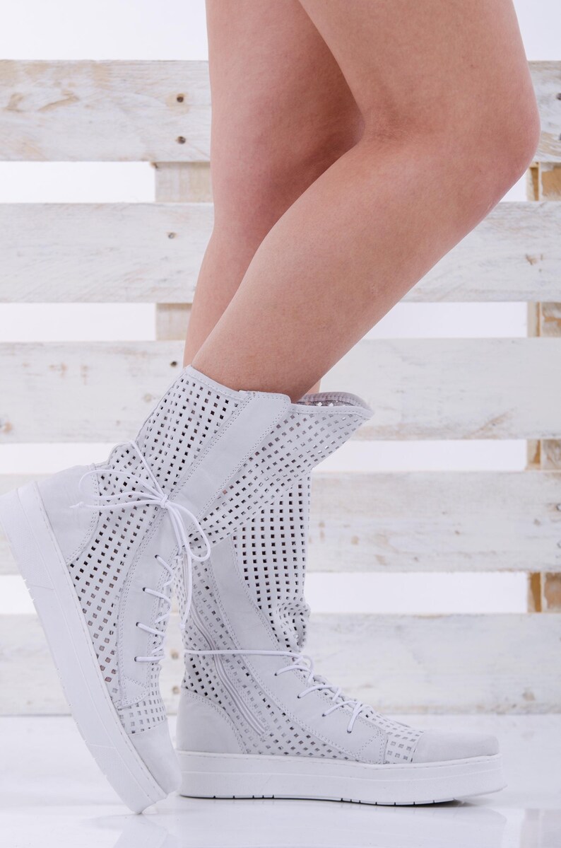 May include: White perforated leather ankle boots with white laces and a white rubber sole.