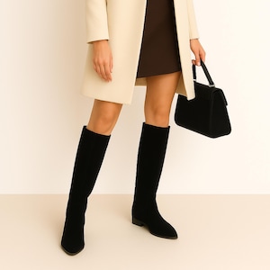 Puede incluir: Botas negras hasta la rodilla con punta y tacón bajo. El conjunto incluye un abrigo color crema, un bolso negro y una falda marrón.