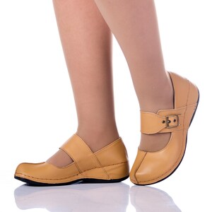 May include: A pair of tan leather shoes with a buckle closure. The shoes have a low wedge heel and are made of a soft, supple leather.