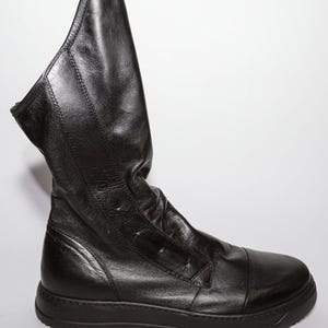 Könnte beinhalten: Schwarze Lederstiefel mit einem lockeren Schaft und einer dicken Gummisohle.