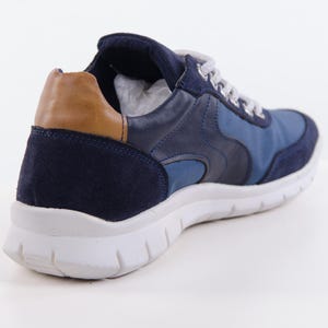 Op de afbeelding: Blauwe su&egrave;de en leren sneakers met een bruine su&egrave;de accent op de achterkant. De sneakers hebben een witte zool.