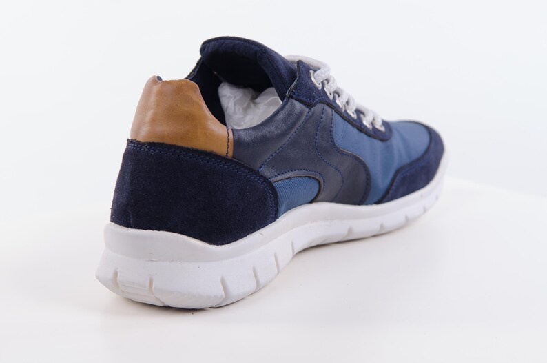 Op de afbeelding: Blauwe su&egrave;de en leren sneakers met een bruine su&egrave;de accent op de achterkant. De sneakers hebben een witte zool.