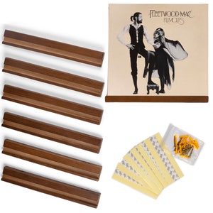 May include: A set of six brown wooden record display shelves with a brown wooden frame and a vinyl record album cover featuring Fleetwood Mac's Rumours album art. The album cover features a black and white photo of the band members. The set also includes adhesive strips and screws for mounting.
