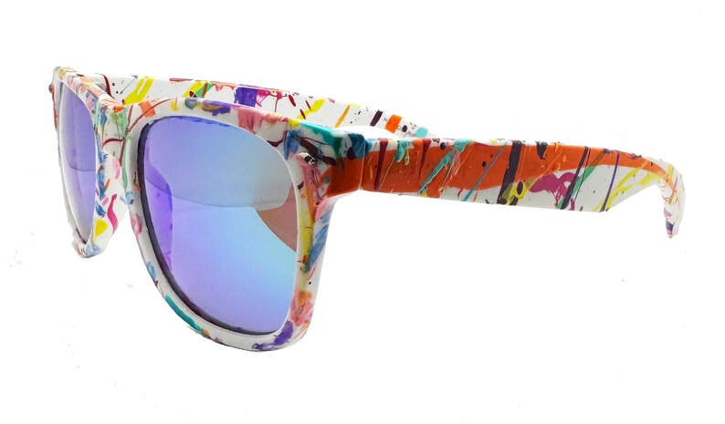 Puede incluir: Gafas de sol con montura blanca y lentes azules. Las monturas est&aacute;n decoradas con salpicaduras de pintura coloridas en naranja, morado, amarillo y verde. Un accesorio de moda.