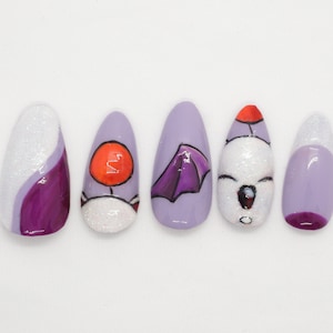 May include: A collection of five artificial nails, each with a unique design. The nails are painted in shades of lavender, white glitter, and purple. Some nails feature cartoon illustrations, including an orange circle, a purple umbrella, and a red hat.