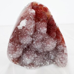Può includere: Una grande geode di agata rossa con un interno cristallino bianco. La geode ha la forma di un cuore e un esterno liscio e lucido.