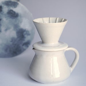 May include: White ceramic pour-over coffee maker with a white ceramic jug. The coffee maker has a cone-shaped filter and a lid.
